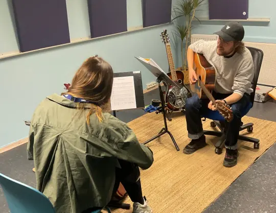Viser bilde av en lærer på kultuskolen skom lærer en elev i individuell opplæring i gitar.