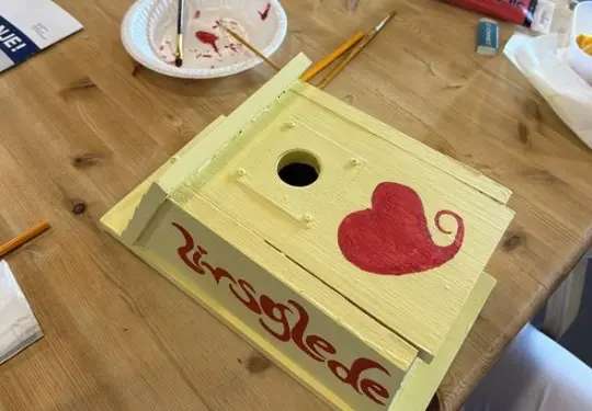 Bilde av noen som har malt ei fuglekasse i gult hvor det er skrevet med rødt Livsglede på.