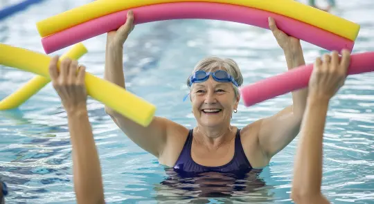 Bilde av ei dame i basseng som smiler og gjør vanngym.