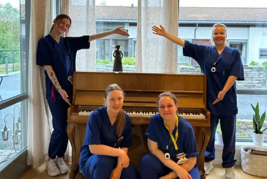 Bilde av fire ansatte foran pianoet