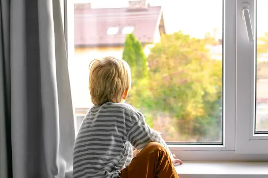 Bilde av et barn som sitter i vinduskarmen og ser ut.