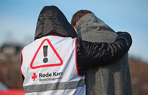 Viser et bilde av en fra Røde Kors med beredskapsvest som hjelper en annen.