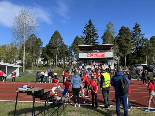 Bilde av en folkemengde og noen som løper under Tinestafetten på friidrettsbana på Tråstad ved KUSK.