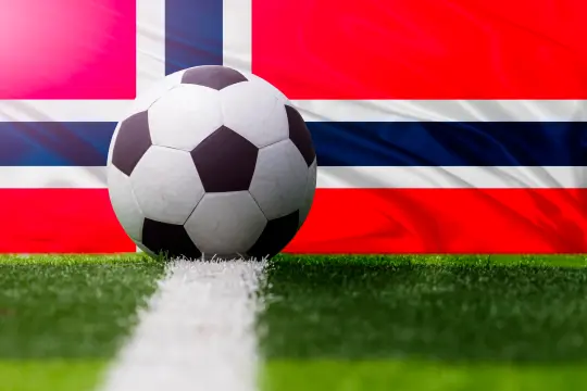 Bilde av en fotball på ei fotballbane med det norske flagget i bakgrunn.