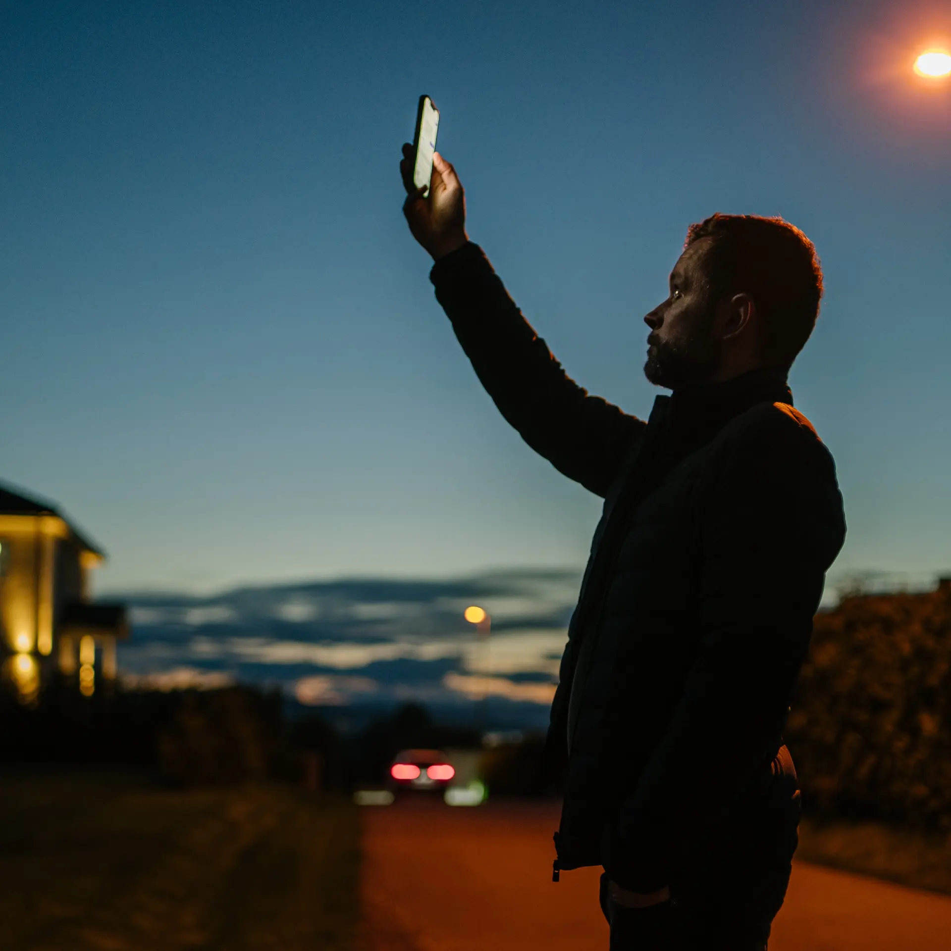 Bilde av en mann som strekker telefonen i været for å lete etter dekning på telefonen.