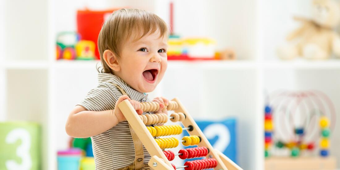 Et barnehagebarn som leker med en leke og ler godt.