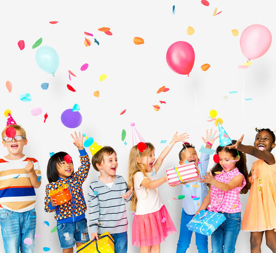 Bilde av 7 barn med bursdagshatter, pakker og ballonger. Alle feirer en bursdag og er glade og ivrige.