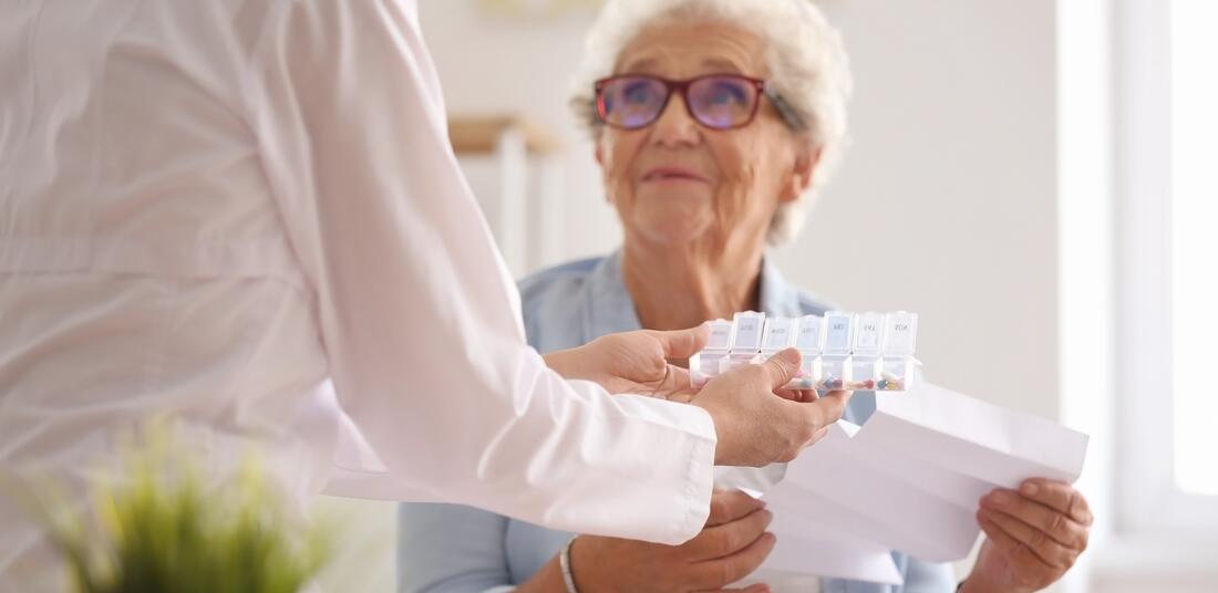 Eldre dame som mottar medisiner hjemme fra en person som jobber innen helse.