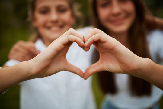 To jenter som sammen danner et hjerte ved å forme hender og fingre.